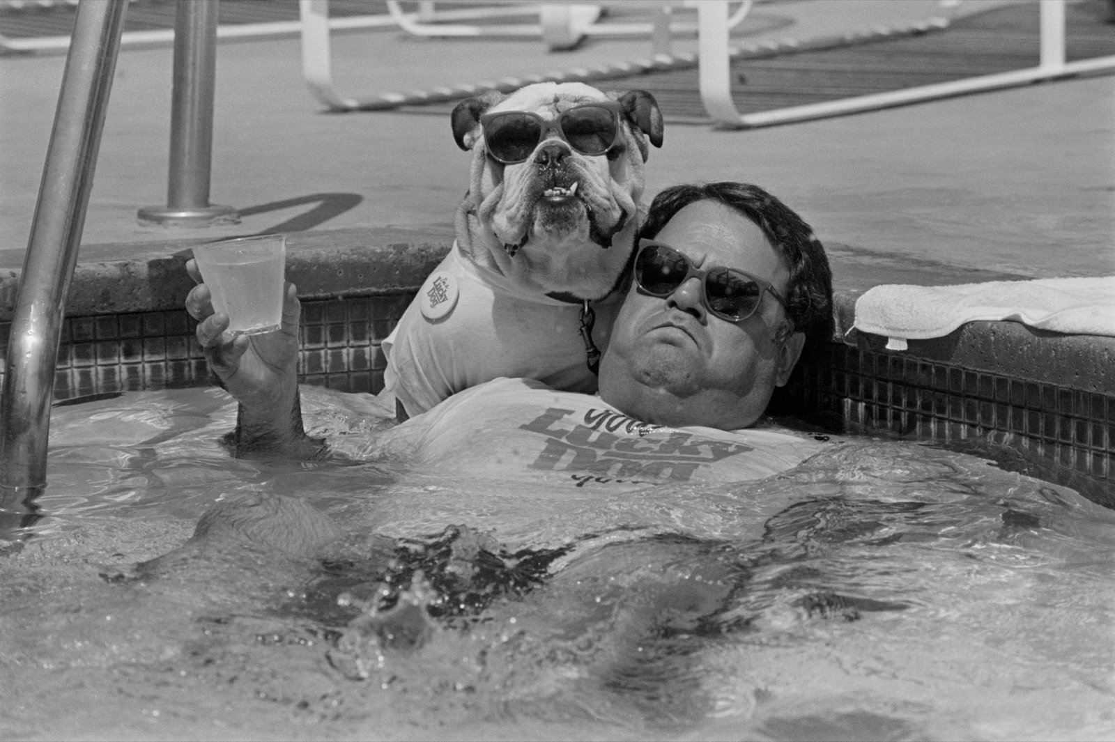 Un hombre y un bulldog con gafas de sol descansando en una piscina